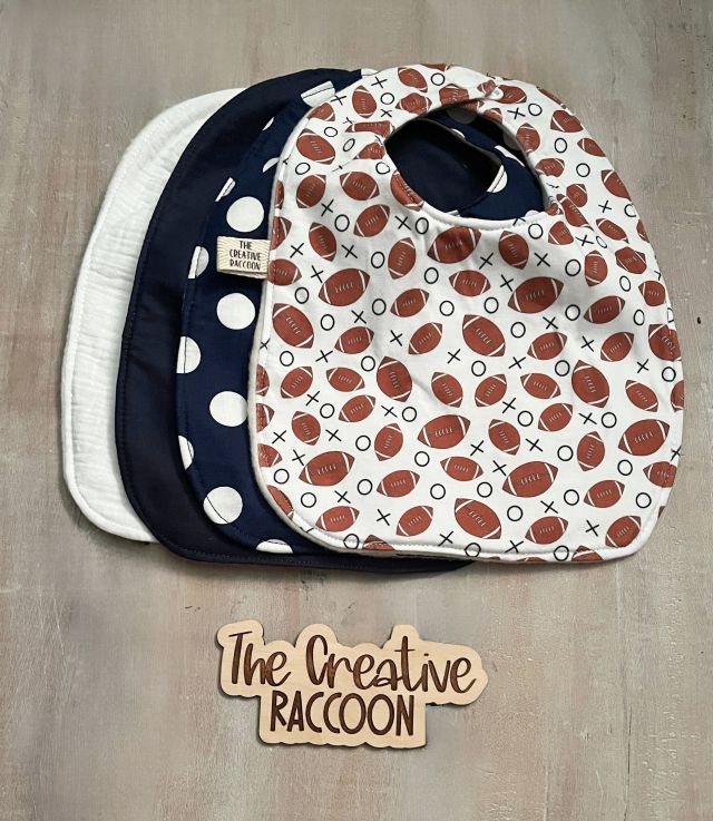 Three baby bibs with different patterns. Solid color bibs - white, & navy blue, patterned baby bibs - football design on white, & navy blue with white dots. Football Baby Gift Sets, Navy Blue Color Theme - The Creative Raccoon
