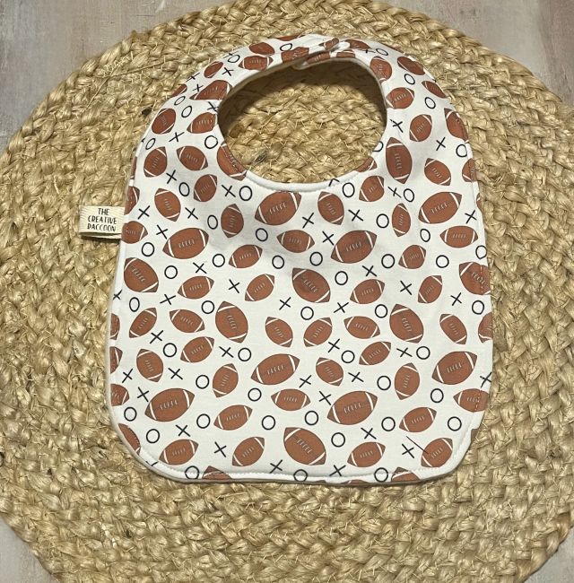 Baby bib with football pattern on a woven mat. football themed baby bibs shown in footballs on a white background. Handmade in Kansas, USA
Football Baby Gift Sets, Kansas Theme - The Creative Raccoon