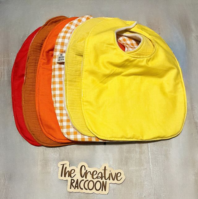 Four colorful bibs stacked on a textured surface with 'The Creative Raccoon' branding. Solid colored baby bibs - red, burnt orange, orange, yellow, and sunshine yellow. Patterned baby bibs - orange and white gingham. Other bibs are available. Handmade in Kansas, USA
Football Baby Gift Sets, Kansas Theme - The Creative Raccoon