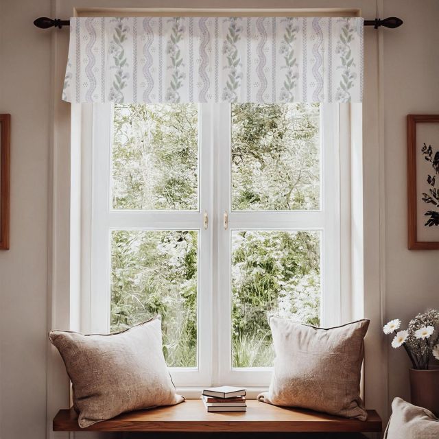 Window with patterned fabric with green leaves and purple flowers on a white background for window valances and a wooden bench with pillows, featuring a view of greenery outside. Window Valance Stripes and Vines, Designer Floral - Pick Your Color - The Creative Raccoon