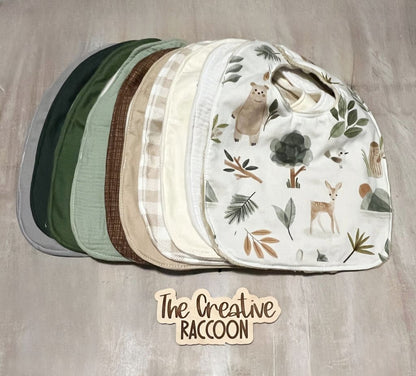 Set of baby bibs with woodland-themed design on a wooden surface, branded 'The Creative Raccoon'. Baby Gift Set Personalized: Woodland Forest Animals - The Creative Raccoon
