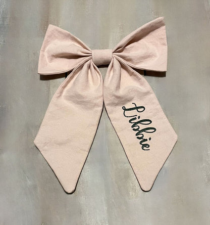 Large pink bow with 'Libbie' embroidered on the bow tail on a gray background. Blush pink bow add-ons for car seat canopy or crib decor. - The Creative Raccoon