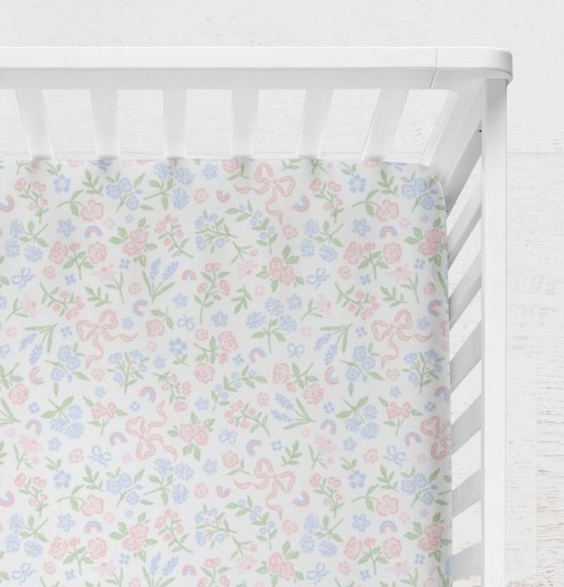 Pastel floral and bow pattern on a white background crib sheet shown on a crib. Bow & Floral Crib Sheet - The Creative Raccoon