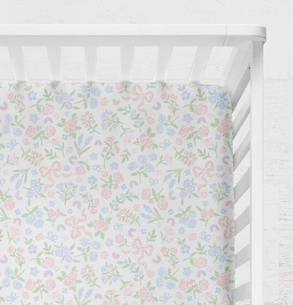 Pastel floral and bow pattern on a white background crib sheet shown on a crib. Bow & Floral Crib Sheet - The Creative Raccoon