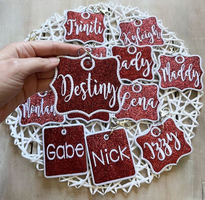 Red glittery name tags with white text on a decorative plate. Custom Cheer Bag Tag, Team Gift Ideas - The Creative Raccoon
