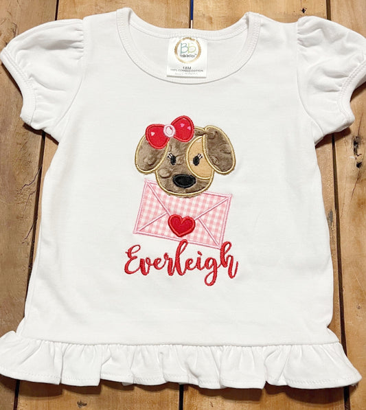 Girl dog Valentine's Day Shirt, embroidered design of a puppy holding an envelope and personalized with child's name. Name shown in Everleigh font. puppy in brown minky, & tan felt. bow red fabric, letter pink & white check.