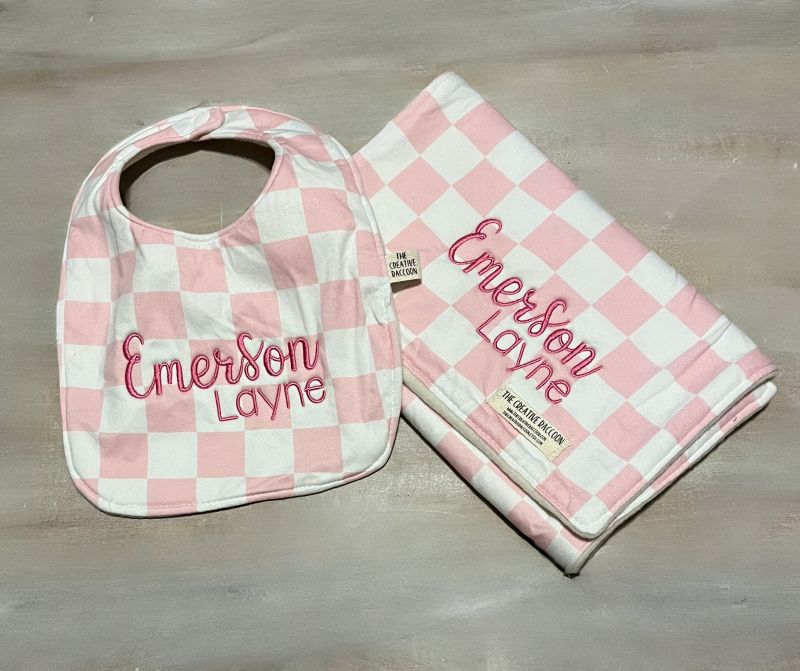 Pink and white checkered bib and burp cloth with 'Emerson Layne' branding on a wooden surface.
Pink Checkered Baby Bib and Burp Cloth Personalized