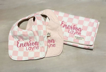 Pink checkered baby bib and burp cloth with 'Emerson Layne' embroidered on both items on a beige surface. Pink Checkered Baby Bib and Burp Cloth Personalized