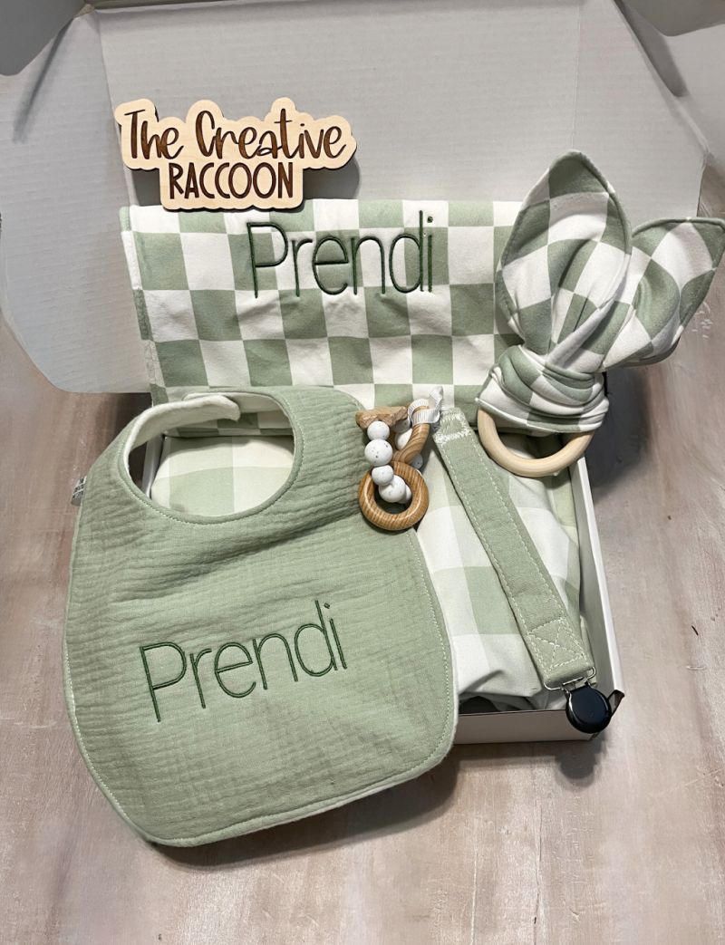 Green bib and checkered burp cloth, pacifier clip, & teether toy with 'Prendi' embroidered on bib and burp cloth. Sage Green Checkered Bib and Burp Cloth Set - the Creative Raccoon