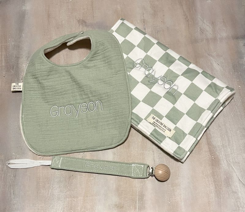 Green bib, green pacifier clip, and checkered burp cloth with 'Grayson' embroider on all items. 
Sage Green Checkered Bib and Burp Cloth Set - the Creative Raccoon
