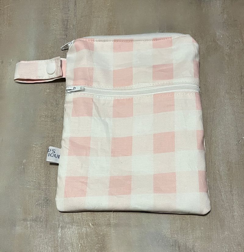 Pink and white checkered pouch with a visible brand tag on a gray surface. Wet Dry Bag, Period Pouch, Checkered Bag - The Creative Raccoon