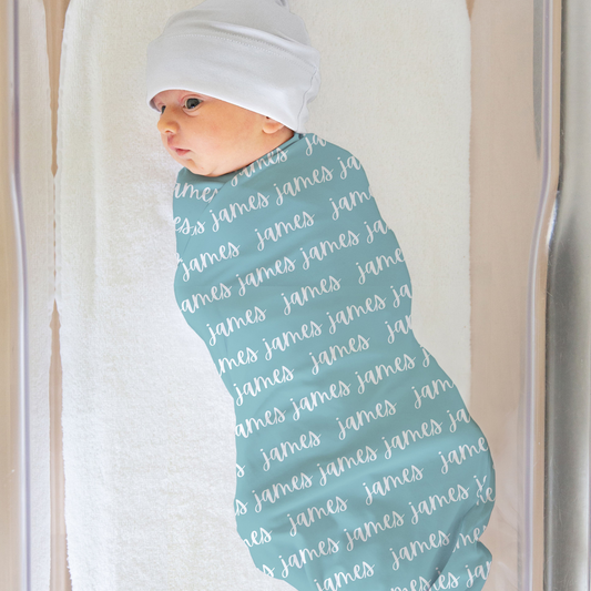 aqua blue swaddle blanket with custom name in white, made out of jersey knit. The design is printed on one side. Blanket shown on a baby in a bassinet