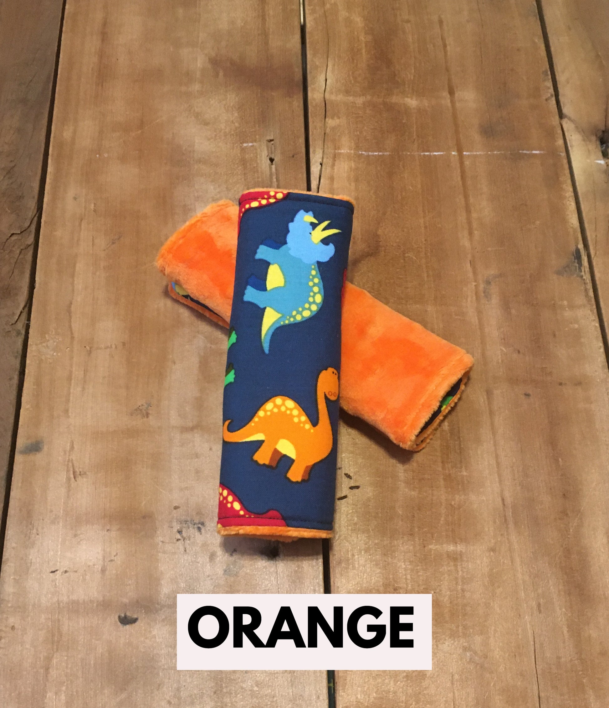 navy dinosaur car seat strap covers - dinosaurs in light blue, orange, red and green shown in 6" size shown with orange minky
