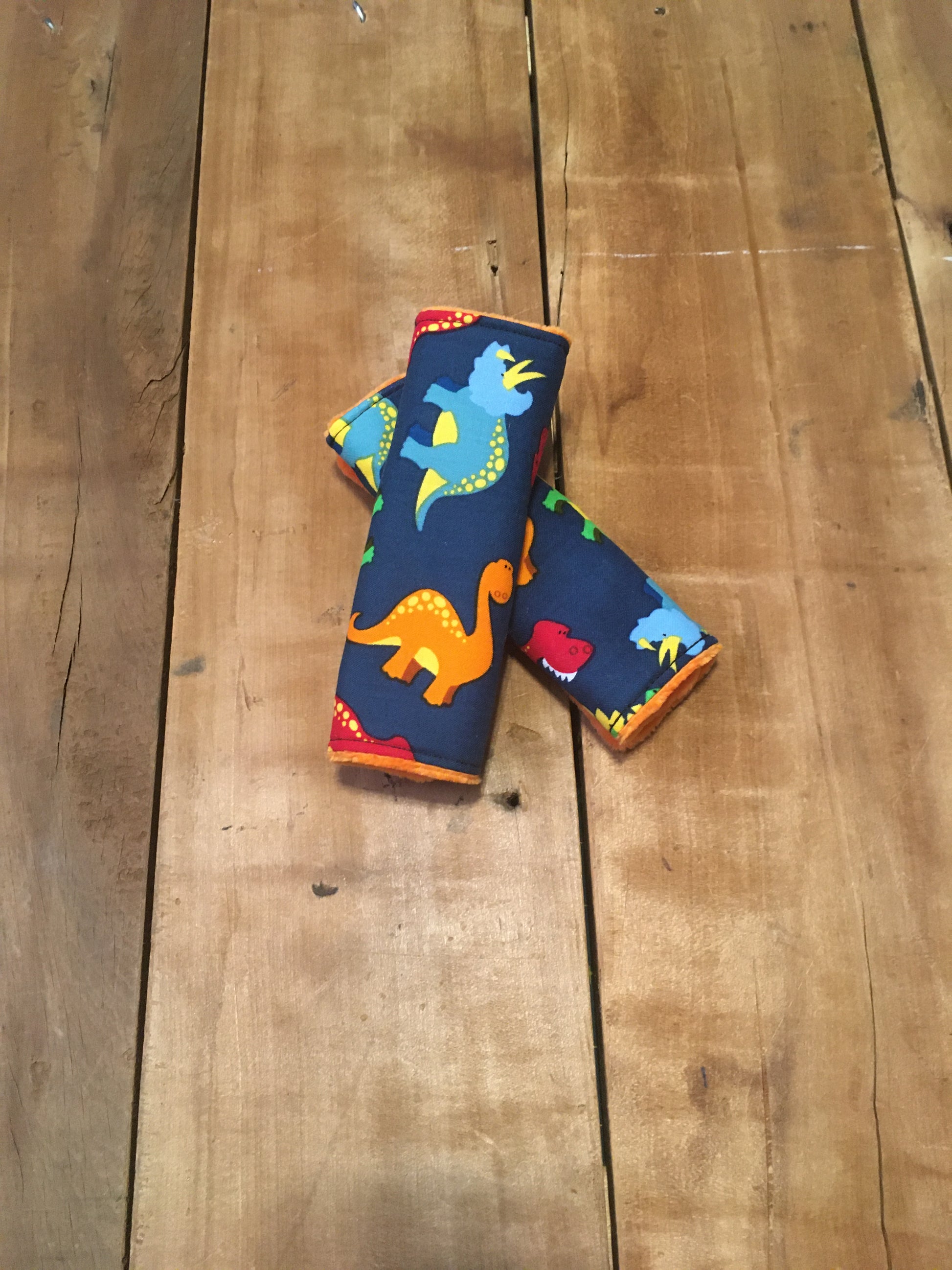 navy dinosaur car seat strap covers - dinosaurs in light blue, orange, red and green shown in 6" size