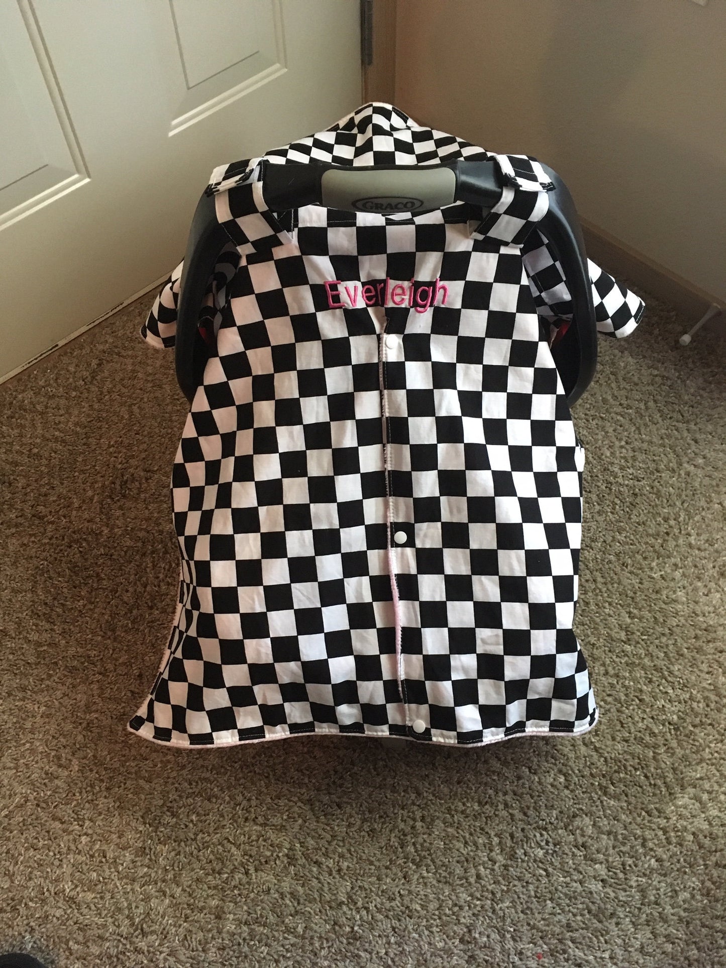 racing check canopy/car seat cover shown in light pink in the open option, shown with snaps closed, and a name (additional fee)
