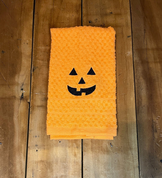 orange towel with pumpkin face embroidered on it.