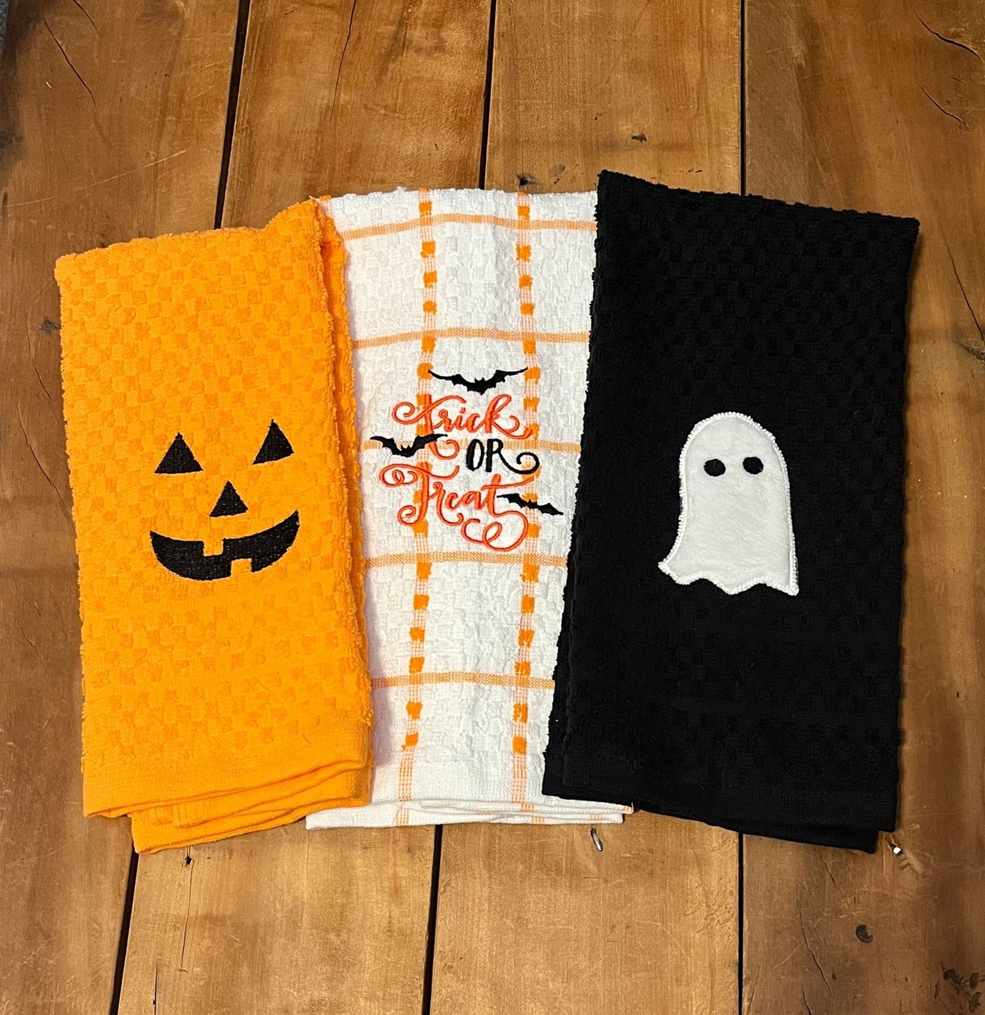 orange pumpkin face towel, orange and white stripe towel with trick or treat and bats, black towel with ghost. embroidered towels