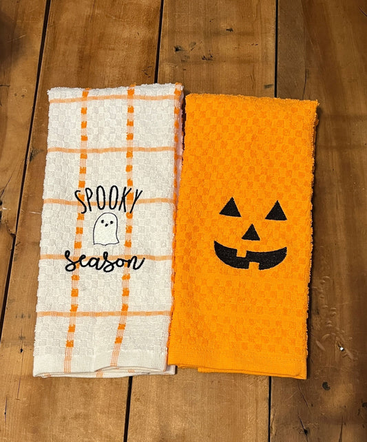 white and orange dish towel with spooky season and a ghost embroidered on the towel, orange towel with pumpkin face embroidered on it.