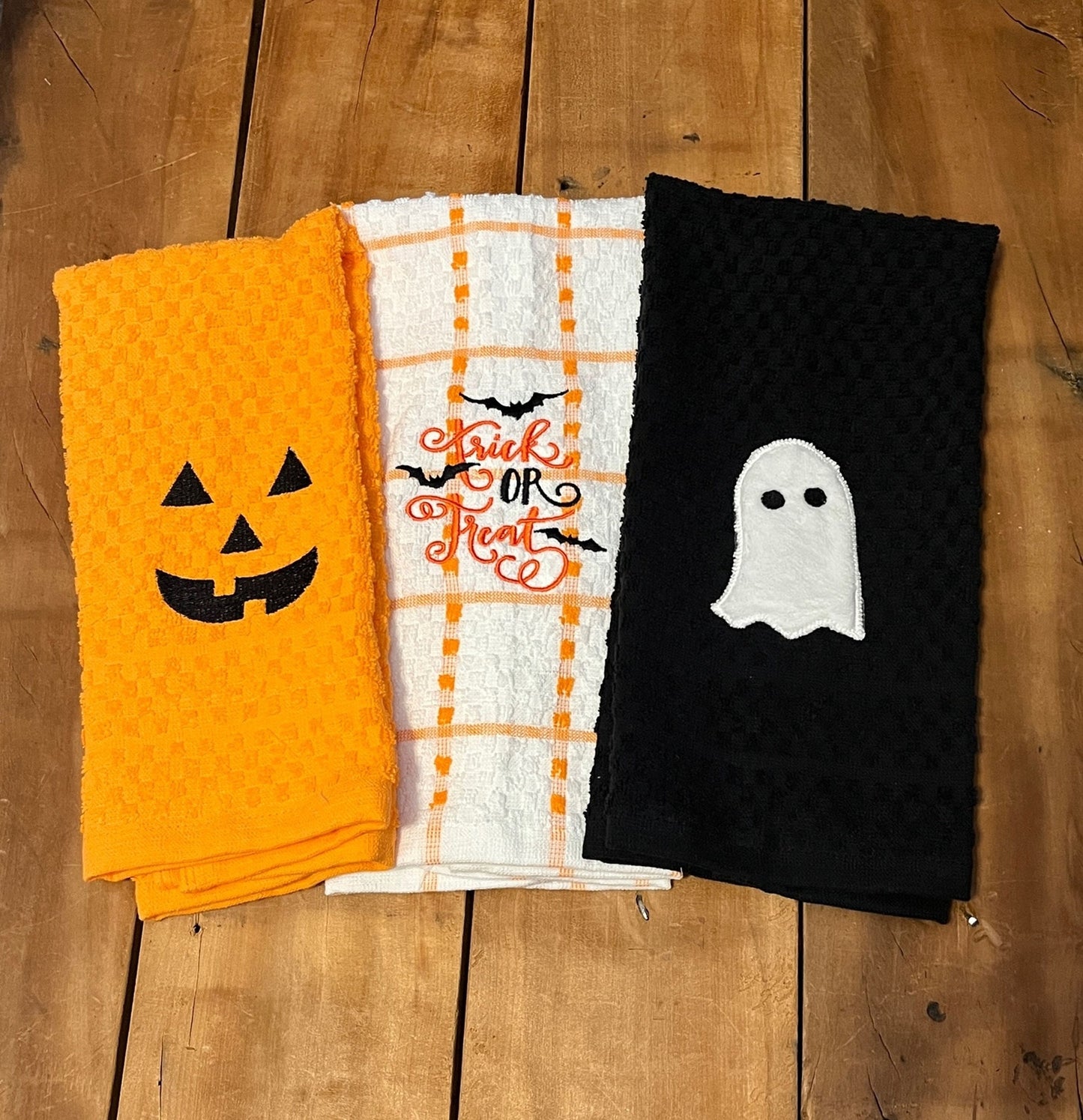 orange pumpkin face towel, orange and white stripe towel with trick or treat and bats, black towel with ghost. embroidered towels